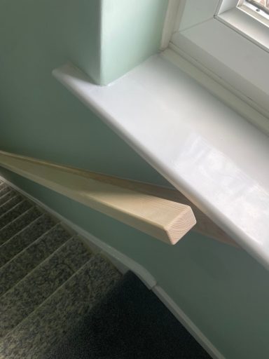 Close-up of a wooden handrail alongside stairs, with a light green wall in the background.