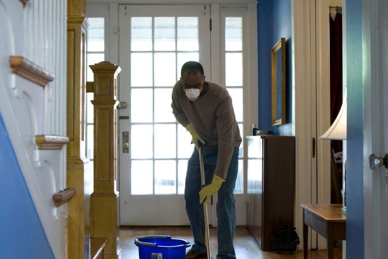 Man cleaning a staircase with a mop and bucket, wearing gloves and a mask.