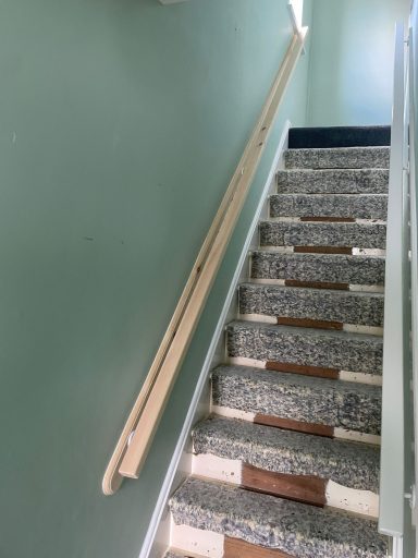 Stairs with a wooden handrail and light green walls, showing patterned grey steps.
