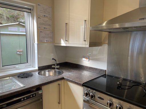 Modern kitchen with a stainless steel sink, stove, and window overlooking an outdoor area.