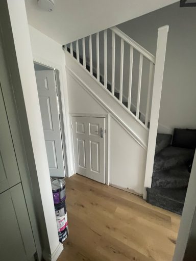 View of a hallway with stairs, a door, and a corner sofa. Wooden floor.