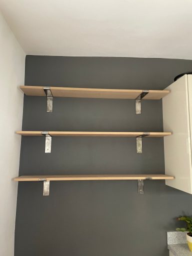 Three wooden shelves mounted on a dark grey wall, with metal brackets for support.
