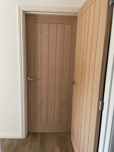 Open wooden door with vertical paneling, leading into a room.
