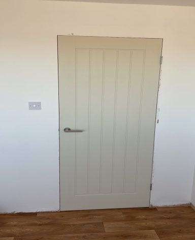 A closed, pale green wooden door with vertical panels against a white wall.