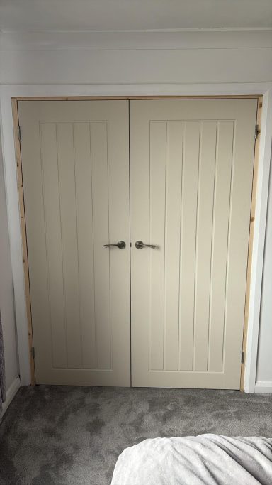 Closed light beige double doors with vertical paneling in a room setting.