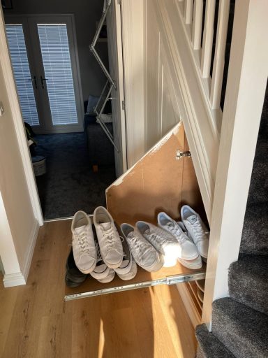 A collection of shoes on a shelf near a staircase and doorway.