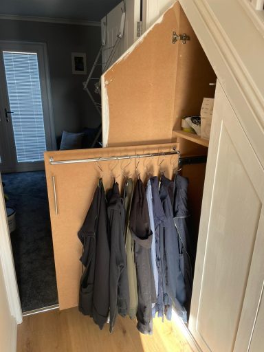 Storage unit under stairs with coats hanging and small shelves above.