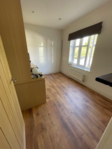 Empty room with wooden flooring, white walls, and a window with a brown blind.