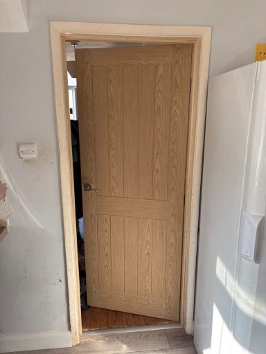 A wooden door in an open frame with light wood finish and a simple design.