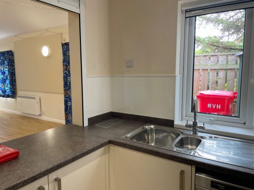 Bright kitchen with a sink, grey worktop, and large window overlooking a garden.