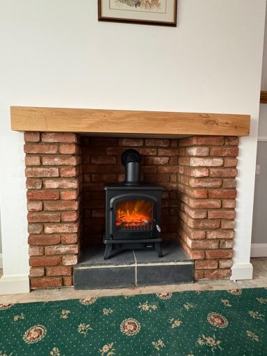 A black stove with a simulated fire, set in a brick fireplace, on a patterned green carpet.