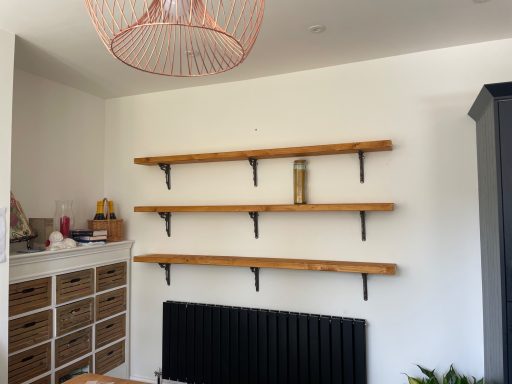 Wooden shelves mounted on a white wall, above a black radiator and storage drawers.