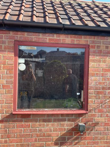 Reflection of a person in a window with a garden view in the background.