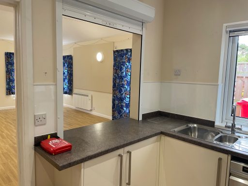 A view of a kitchen with a countertop looking into a brightly lit room with blue curtains.