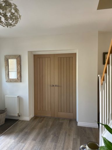 Wooden double doors in a well-lit hallway with a mirror and staircase.