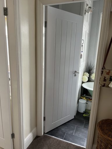 Open white door leading to a small room with a sink and light-coloured flooring.