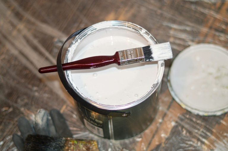 White paint in a can with a brush resting on top, set on a protective surface.