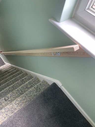 Handrail along a staircase, with light green walls and a window nearby.