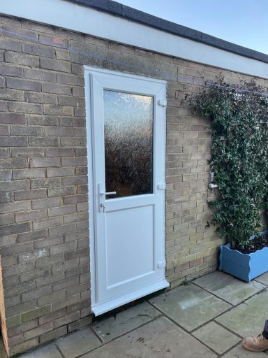 White door with a frosted glass panel, set in a brick wall with plants nearby.