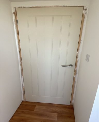 A plain cream door with vertical paneling in a light-coloured hallway.