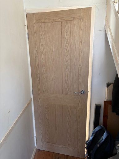 Plain wooden door with vertical panels, located in a narrow hallway.