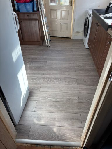 Light wooden flooring in a kitchen, with cabinets and appliances visible in the background.