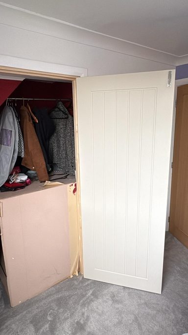 Open wardrobe door revealing clothes and a partially visible room corner.