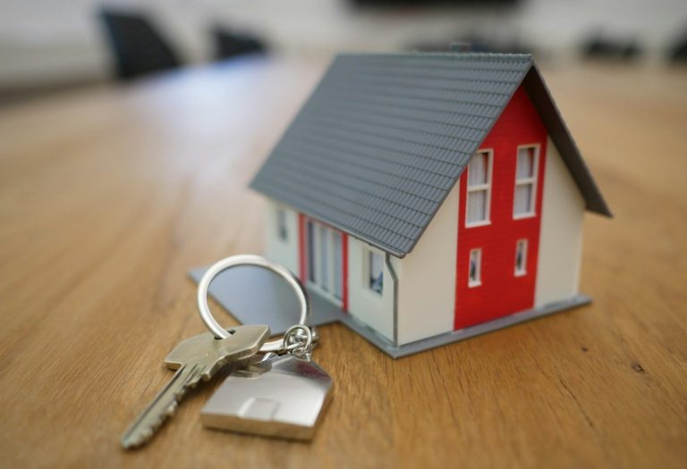 Model house with a red door beside a set of keys on a wooden surface.