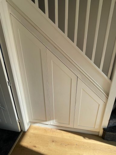 White wooden door with panelling beneath a staircase, on light wooden floor.