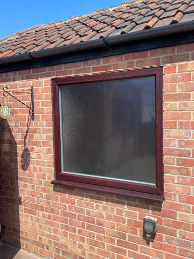 A large brown-framed window on a brick wall with a roof in the background.