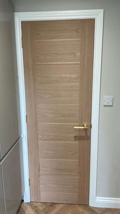 Interior wooden door with a light wood finish and a simple horizontal panel design.