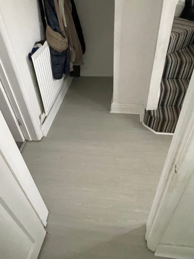 A hallway with light grey flooring and white doors, leading to a darker area.