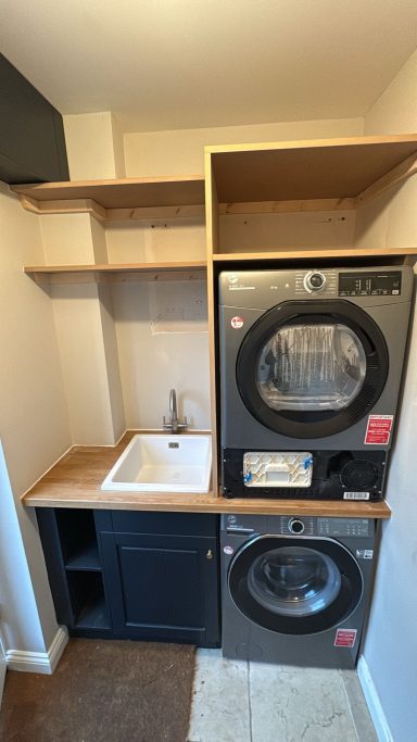 A laundry area featuring stacked washer and dryer, sink, and wooden shelves.
