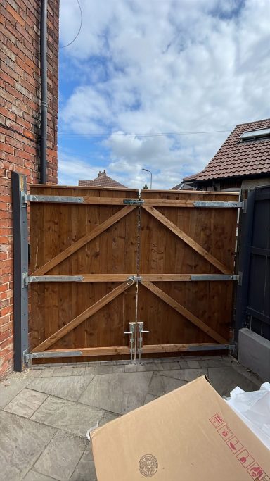 Brown wooden gate with metal framing, set against a cloudy sky.